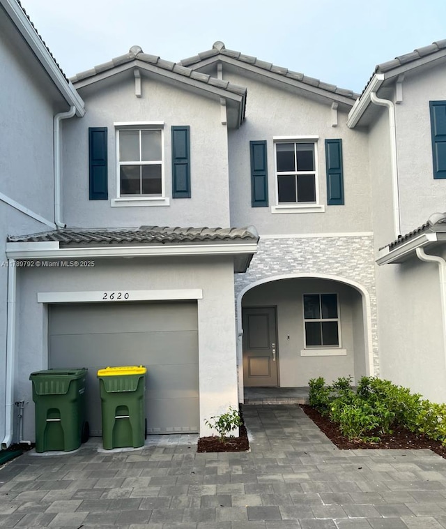 doorway to property featuring an attached garage, a tile roof, and stucco siding
