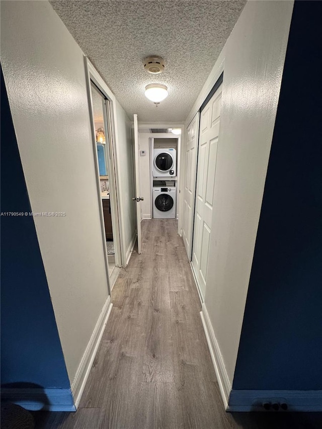 hall with stacked washer / drying machine, wood finished floors, a textured ceiling, and baseboards
