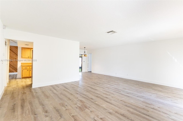 unfurnished room with a chandelier, light wood-style floors, and baseboards