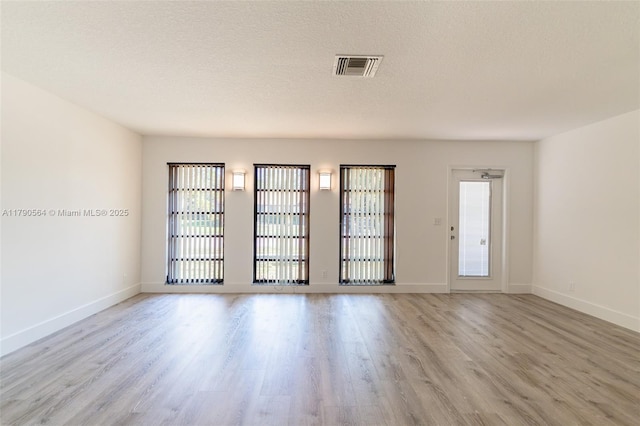 spare room featuring light wood-style flooring, healthy amount of natural light, baseboards, and a textured ceiling