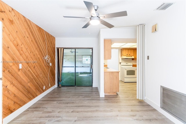 empty room featuring ceiling fan, light wood-type flooring, wood walls, and baseboards