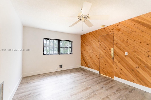spare room featuring baseboards, wood walls, ceiling fan, and light wood-type flooring