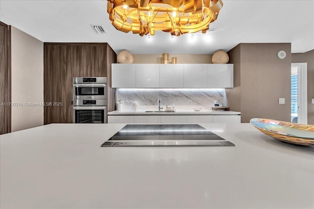 kitchen with light countertops, cooktop, double oven, and a sink