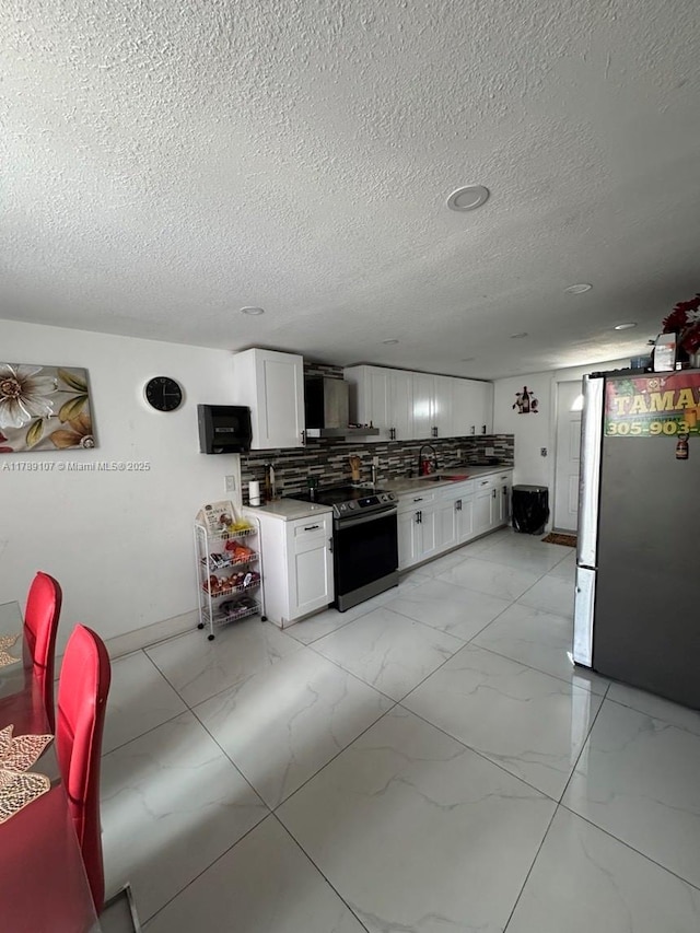 kitchen with range with electric stovetop, freestanding refrigerator, light marble finish floors, white cabinets, and a textured ceiling