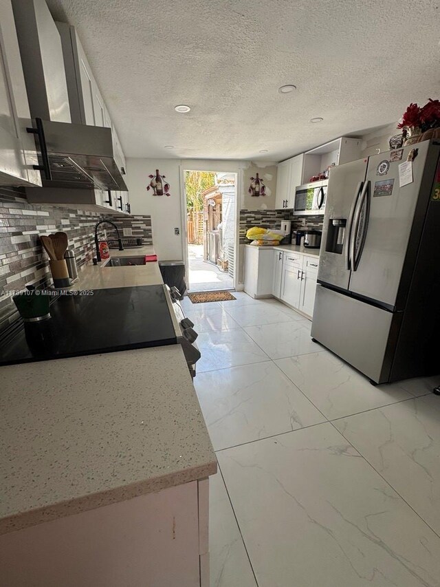 kitchen featuring wall chimney exhaust hood, decorative backsplash, marble finish floor, and appliances with stainless steel finishes
