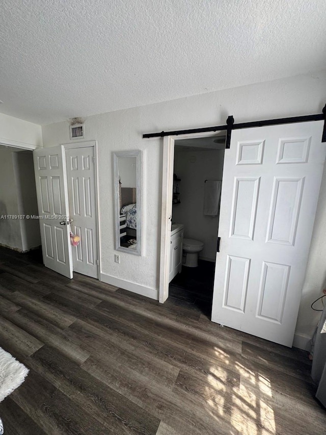 unfurnished bedroom with a barn door, a textured ceiling, dark wood-type flooring, and ensuite bathroom