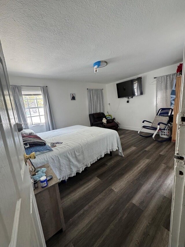 bedroom with baseboards, a textured ceiling, and dark wood finished floors