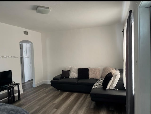 living area featuring wood finished floors, baseboards, visible vents, and arched walkways