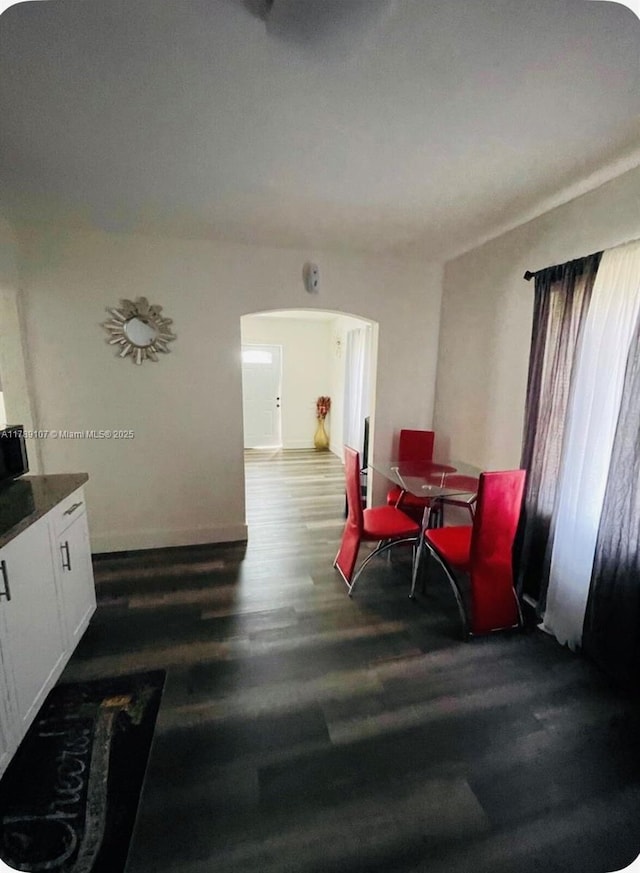 dining area with wood finished floors, arched walkways, and baseboards