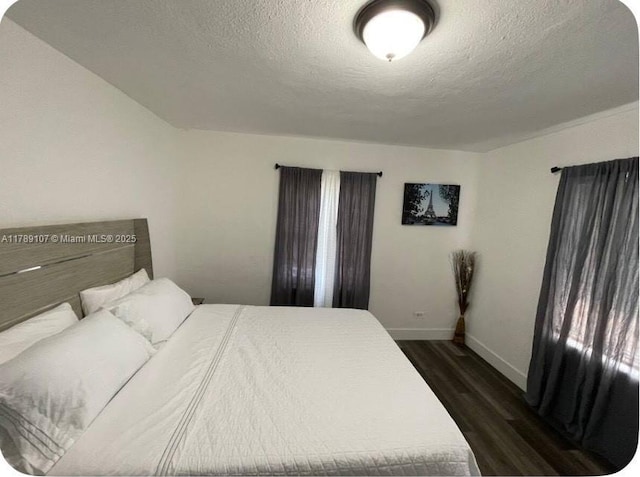 bedroom with dark wood-style floors, a textured ceiling, and baseboards