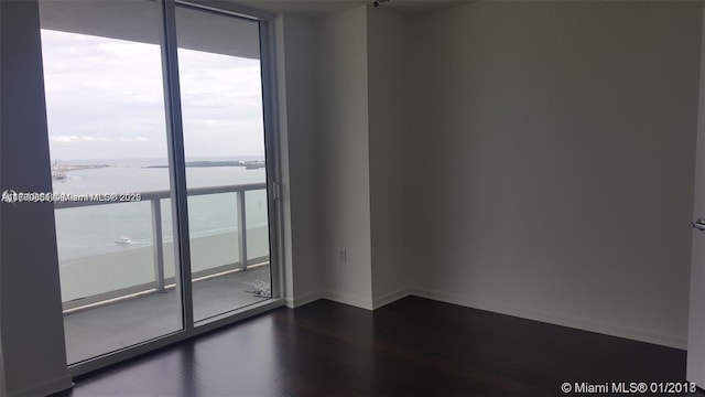 empty room featuring dark wood-type flooring, a water view, and floor to ceiling windows