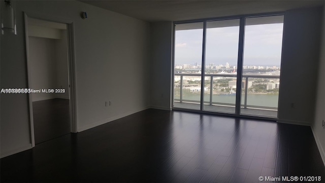 empty room with a view of city, baseboards, a wall of windows, and dark wood finished floors