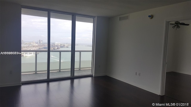 empty room featuring dark wood-style floors, visible vents, ceiling fan, and expansive windows