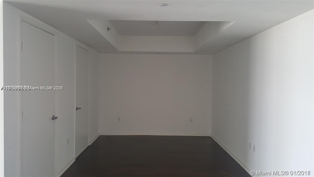 corridor with a raised ceiling and dark wood finished floors
