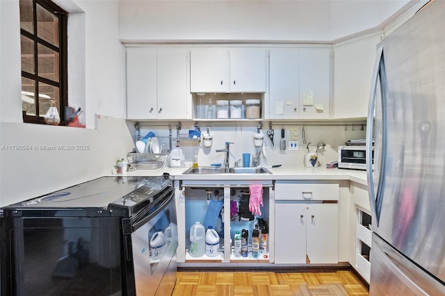 kitchen featuring electric stove, freestanding refrigerator, light countertops, a sink, and white cabinetry