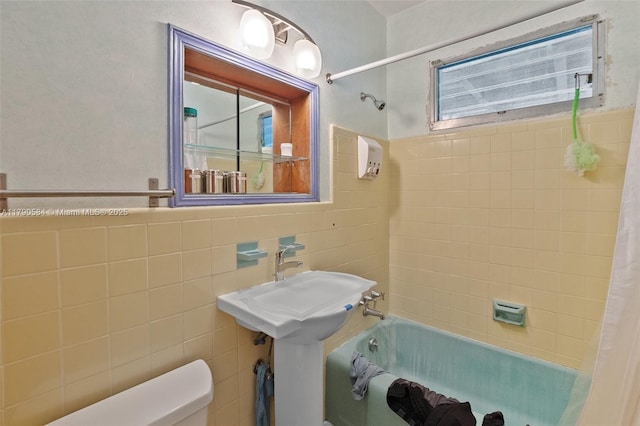 bathroom featuring toilet, tile walls, wainscoting, and shower / tub combo