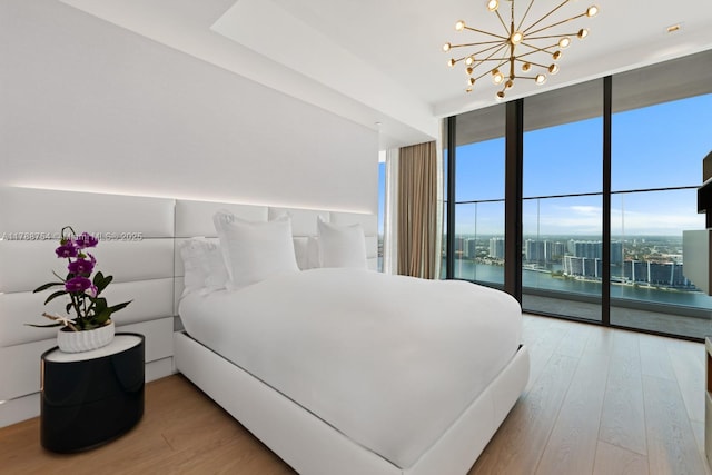 bedroom featuring a wall of windows, access to outside, a water view, a chandelier, and light wood finished floors
