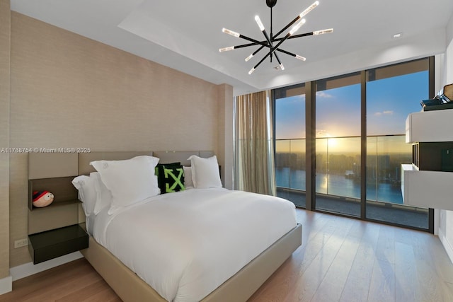 bedroom featuring access to outside, a notable chandelier, a wall of windows, baseboards, and wood finished floors