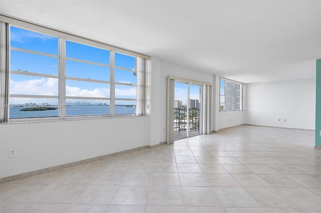 11930 N Bayshore Dr Unit 1007, North Miami, FL 33181 - empty room with light tile patterned floors, a textured ceiling, a water view, and baseboards