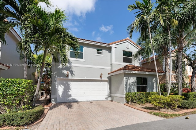 mediterranean / spanish-style house featuring a garage, stucco siding, decorative driveway, and a tile roof
