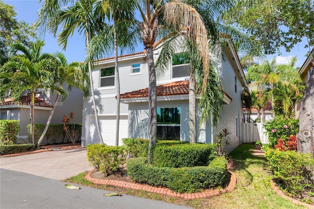 mediterranean / spanish-style house with a tiled roof, a garage, decorative driveway, fence, and stucco siding