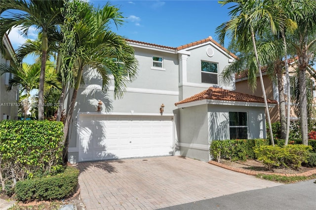 mediterranean / spanish-style house with decorative driveway, an attached garage, a tile roof, and stucco siding