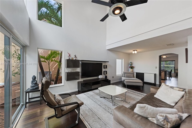 living area with a ceiling fan, a towering ceiling, arched walkways, wood finished floors, and baseboards