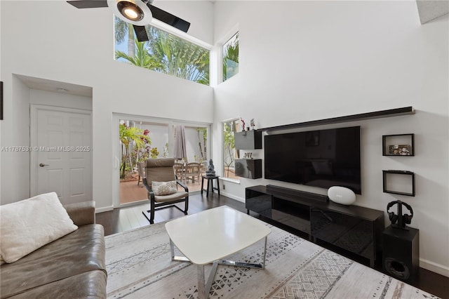 living room with wood finished floors, a ceiling fan, a wealth of natural light, and a towering ceiling