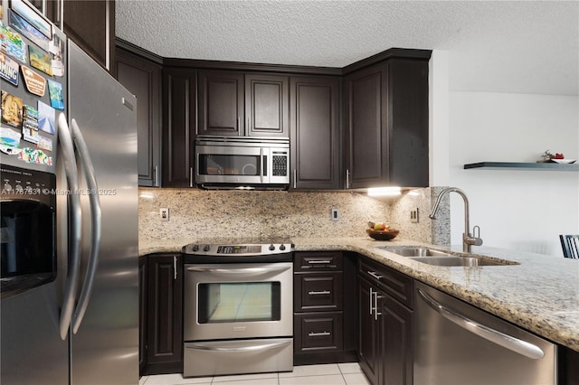 kitchen featuring light stone countertops, appliances with stainless steel finishes, a sink, decorative backsplash, and light tile patterned floors