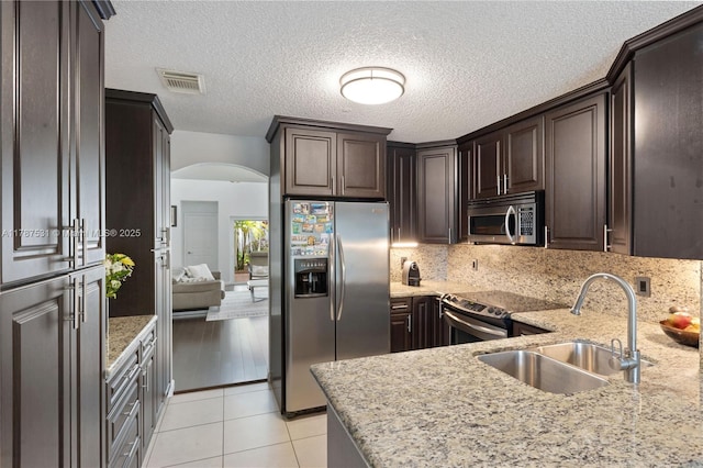 kitchen with dark brown cabinets, a sink, arched walkways, stainless steel appliances, and visible vents