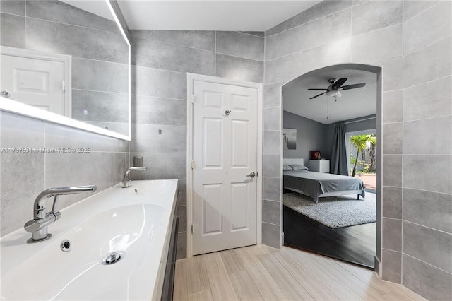 bathroom featuring vanity, ensuite bath, a ceiling fan, tile walls, and wood finished floors