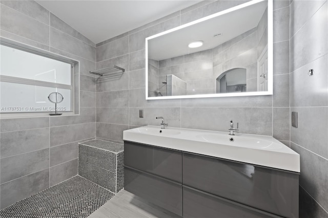 bathroom with a sink, tile walls, double vanity, and tiled shower
