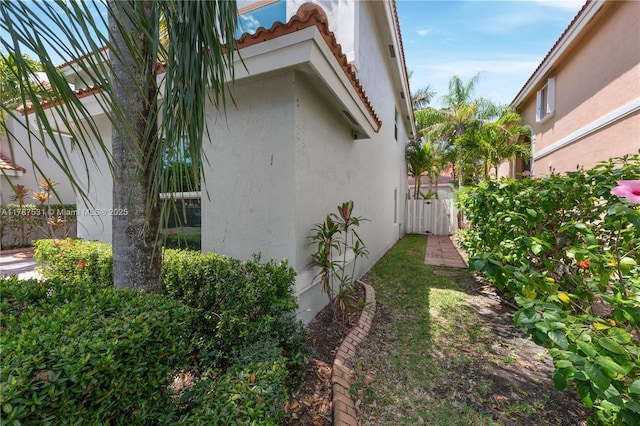 view of side of property featuring a tiled roof, fence, a gate, and stucco siding