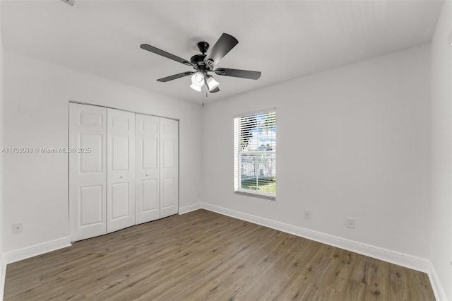 unfurnished bedroom featuring baseboards, wood finished floors, a ceiling fan, and a closet