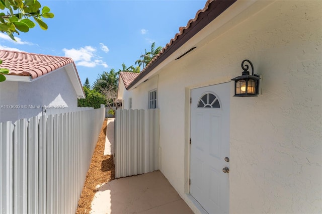 doorway to property with fence, stucco siding, and a tile roof