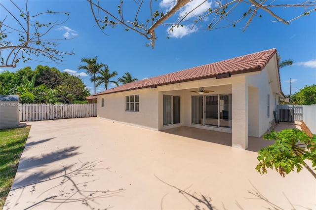 rear view of house with a tile roof, ceiling fan, stucco siding, and fence