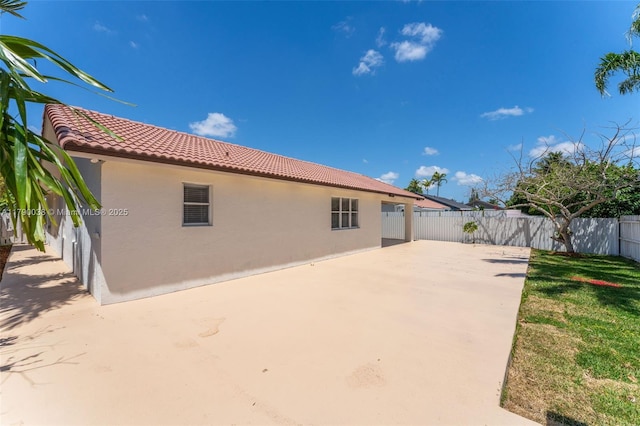 rear view of house with stucco siding, a patio, fence private yard, and a tile roof