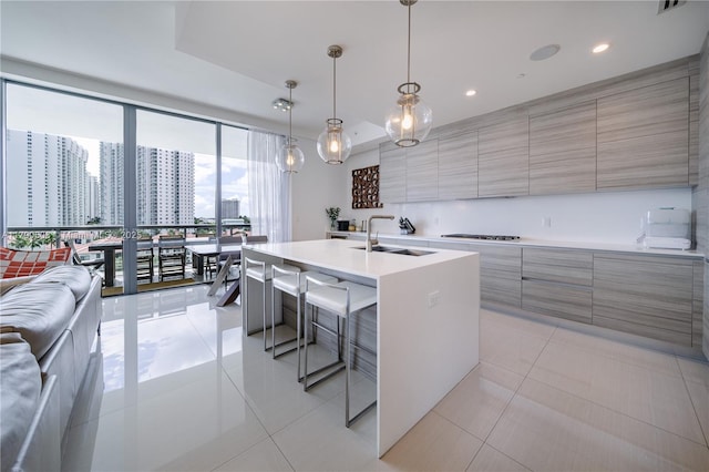 kitchen featuring modern cabinets, a sink, a kitchen bar, light countertops, and an island with sink