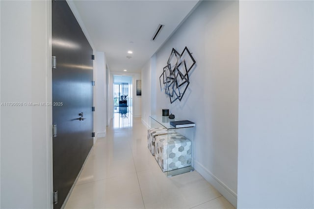 corridor with baseboards, visible vents, and light tile patterned floors