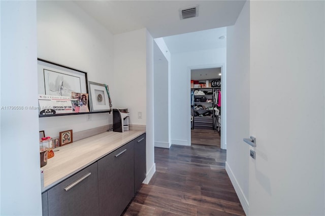 hall featuring dark wood-style flooring, visible vents, and baseboards