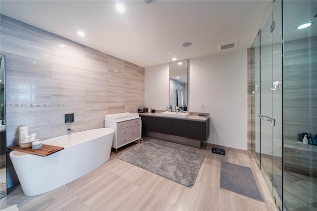 bathroom with a shower stall, tile walls, vanity, a soaking tub, and visible vents