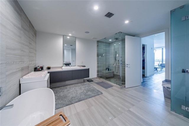 full bath featuring a shower stall, tile walls, a freestanding tub, vanity, and visible vents