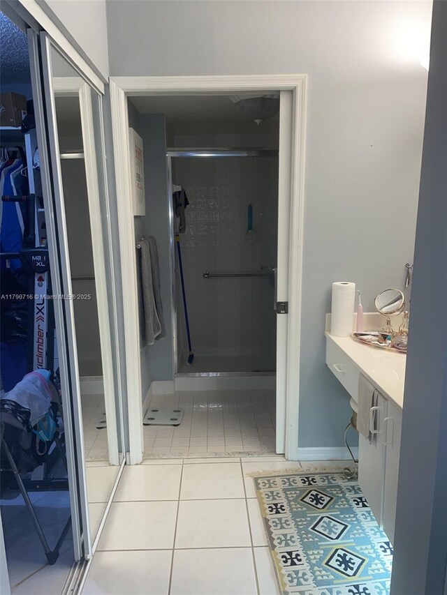 full bath featuring tile patterned floors, a shower stall, a walk in closet, vanity, and baseboards