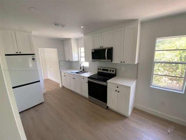 kitchen featuring freestanding refrigerator, a sink, baseboards, light countertops, and electric stove