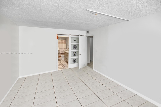 unfurnished room featuring visible vents, a barn door, a textured ceiling, and baseboards