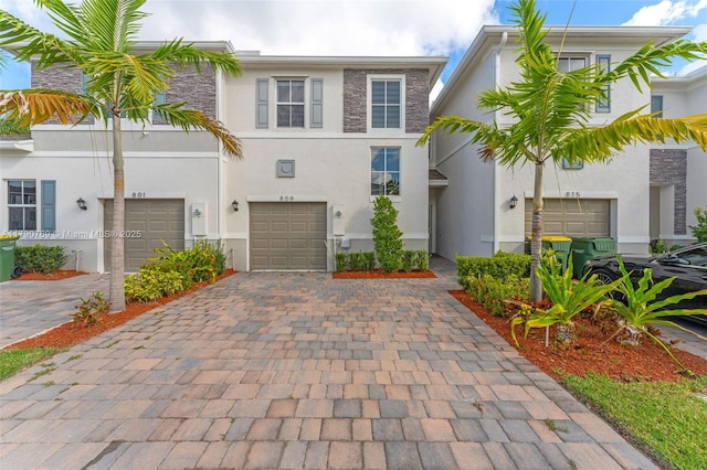 view of property featuring an attached garage, stone siding, decorative driveway, and stucco siding
