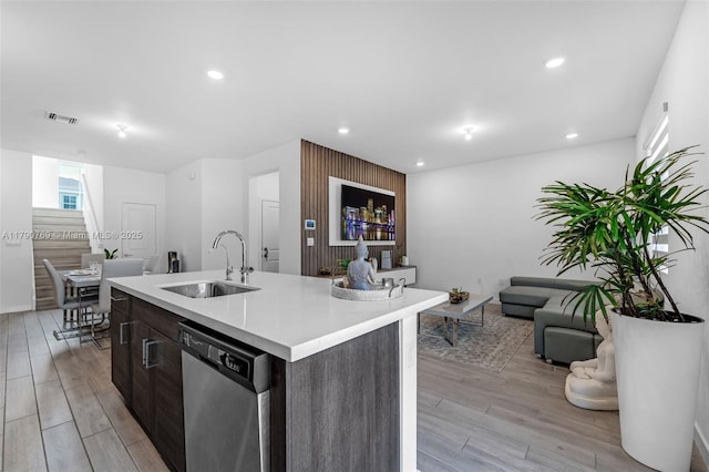 kitchen with stainless steel dishwasher, a sink, visible vents, open floor plan, and light wood-type flooring