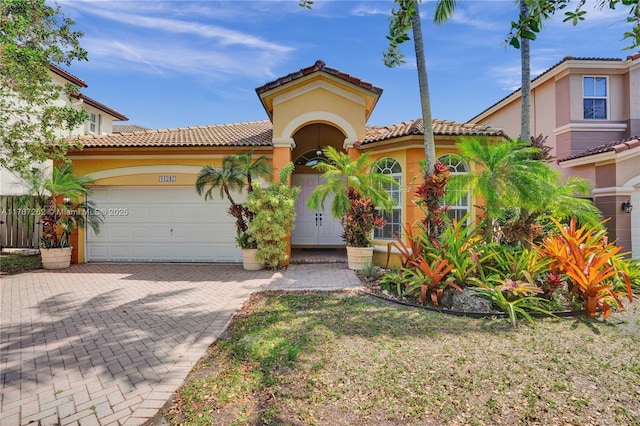 mediterranean / spanish-style house featuring decorative driveway, a garage, stucco siding, and a tiled roof