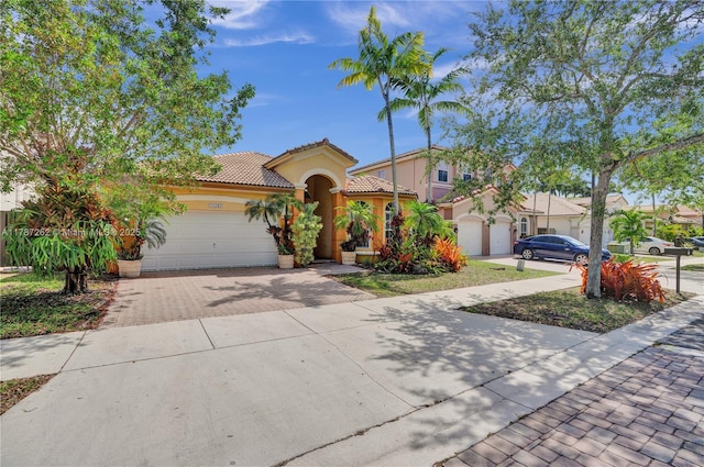 mediterranean / spanish home with a tile roof, decorative driveway, stucco siding, and a garage