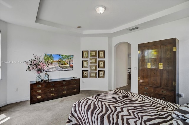 carpeted bedroom with baseboards, visible vents, arched walkways, and a tray ceiling